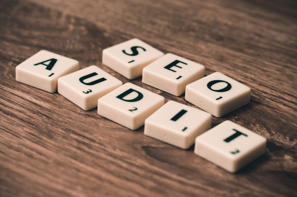 Letter tiles spelling out the words "SEO AUDIT" arranged diagonally on a textured wooden surface.